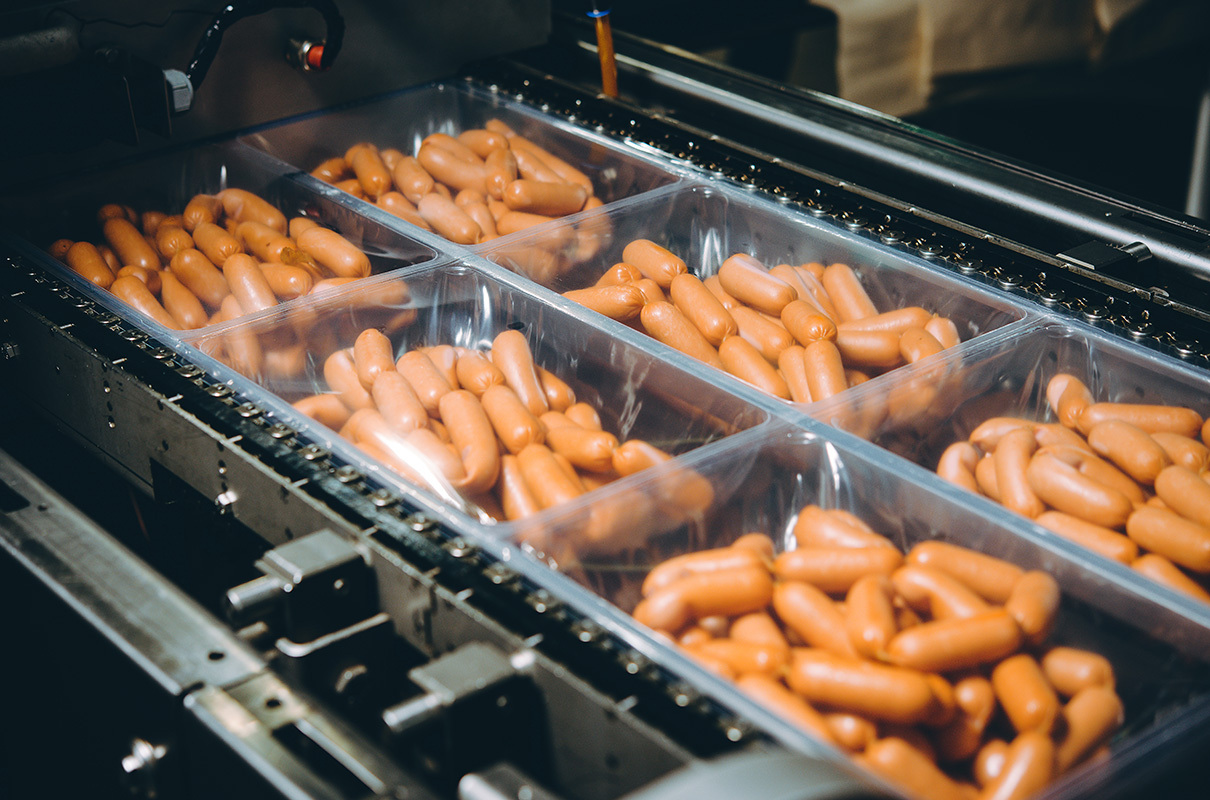 Containers of sausage moving through a machine being inspected for contaminates