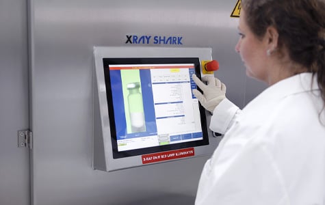 A caucasian woman in a white lab coat pushing buttons on the digital display screen of a stainless steel machine.